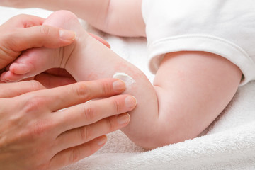 Fototapeta Woman hand holding infant leg. Mother carefully applying medical ointment. Red dry skin allergy from milk formula or other food. Care about baby body. Closeup. obraz