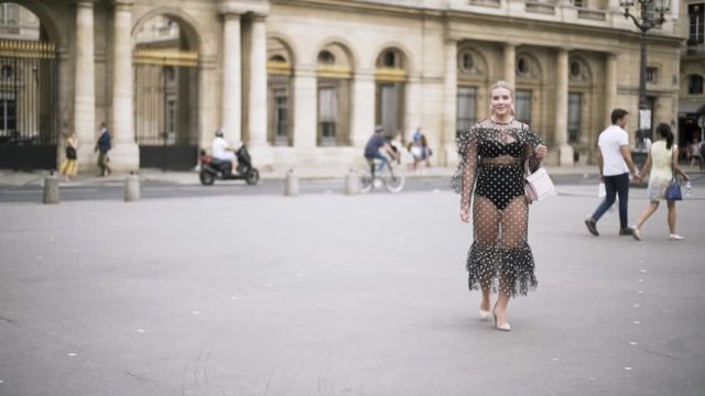 Young pretty woman with blond hair in front of a big historic building, France, travelling in Europe. Action. Sexy lady wearing chiffon dotted dress walking in the street.