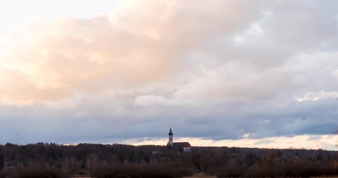 Time lapse of moving clouds during sunset above a landscape with the church of Diessen in the middle in Bavaria, Germany