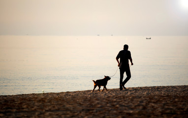 Man walking leash dog for a walk at dawn on the beach, happily