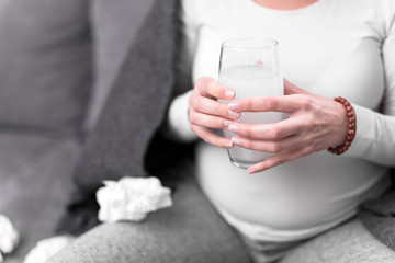 Pregnant woman taking vitamin tablet in a glass of water.