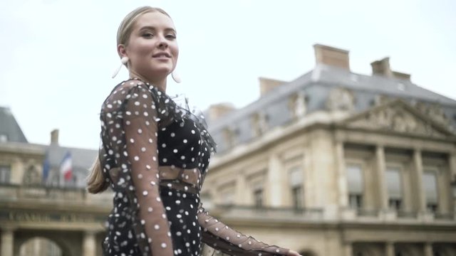Stylish European woman wearing black dotted sexy dress and white small purse, Paris, France. Action. Blond plus size model walking in the street.