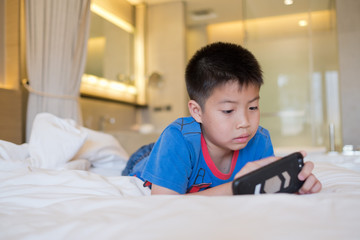 asian chinese boy playing smartphone on bed, kid use phone and play game, addicted game and cartoon, 