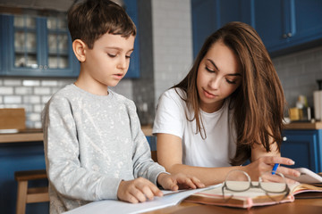 Image of nice woman and cute boy reading exercise while doing homework