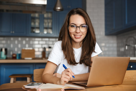 Image of smiling nice woman working with laptop and writing