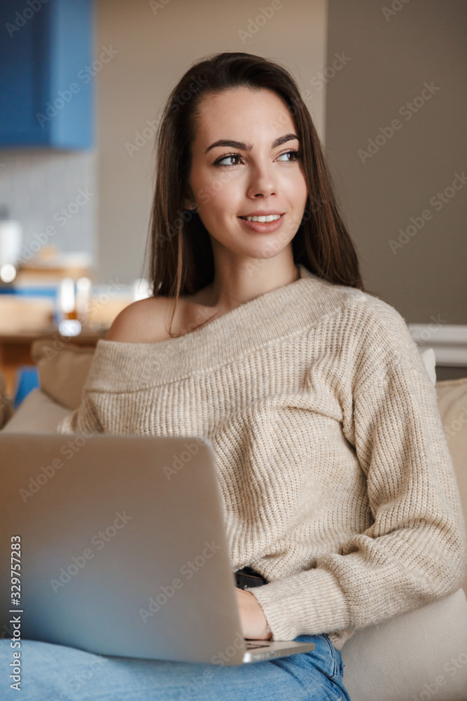 Poster Image of joyful woman smiling and using laptop while sitting on couch