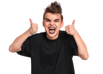 Portrait of teen boy with spooking make-up thumbs up gesture, isolated on white background. Caucasian young teenager in style of punk goth dressed in black screaming and showing success sign.