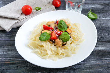 Pasta with mussels, tomatoes on a white plate on a wooden background. Top view.