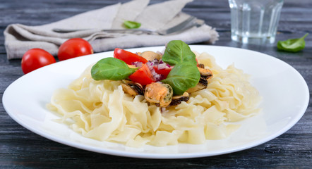 Pasta with mussels, tomatoes on a white plate.