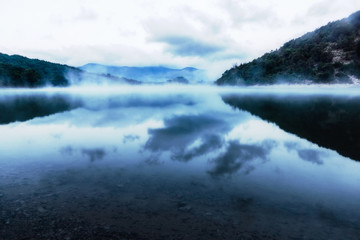 Mountain lake in the early morning. The sun has not yet risen. smoke above the water. In the distance the blue mountains