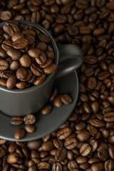 Fototapeta premium Cup and saucer with coffee beans on coffee background. View from above close-up.
