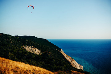 Paraglider flies in the blue sky over the blue sea and green mountains