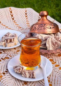 Turkish tea in a glass Cup and marble halva on a table with a handmade tablecloth and candy maker on a Sunny day