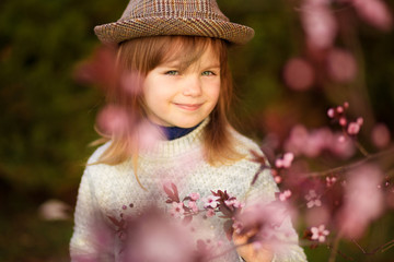 Spring portrait, adorable little girl in hat walk in blossom tree garden