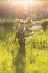 little child holds in his hand a water bottle on sunset background