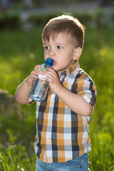 handsome boy drinks clear water from a bottle on a sunny day outside