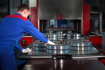 A worker in the production of bearings manually removes the finished product after canning it with engine oil. Photo without a face from the back. Out of focus. Photos at the factory - obrazy, fototapety, plakaty