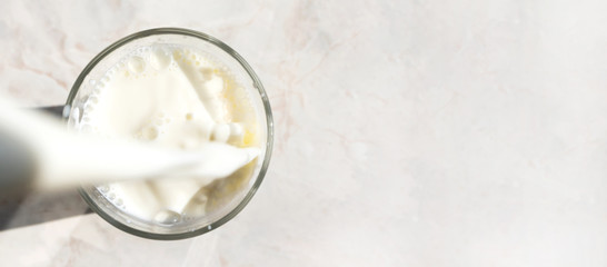 Freshness milk filling glass on marble table background with copy space, above. Drink splash, close-up. Dairy product banner format