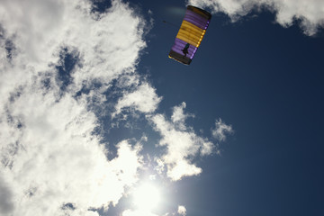 Bright canopy of a parachute against a background of clouds illuminated by the sun and a blue sky.