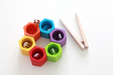 Bright rainbow coloured educational wooden toy. Preschool game for toddlers. Colourful beehive with bees and tweezers to develop fine motor skills.