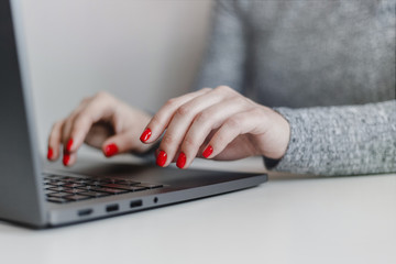 Closeup of woman's hands with red nails on the grey laptop keyboard. Young businesswoman working in an office on a computer. Business, industry and job concept.