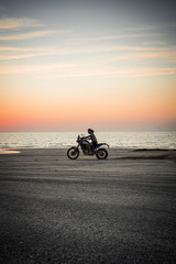 Obraz na płótnie Canvas Masirah Island, Oman, January 1, 2020: Man on a motorcycle on the beach at sunset