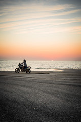 Fototapeta na wymiar Masirah Island, Oman, January 1, 2020: Man on a motorcycle on the beach at sunset