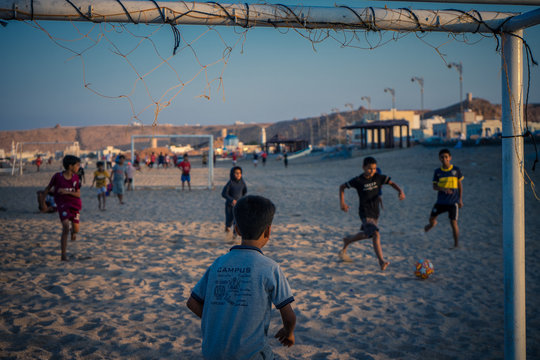 Sur, Oman, January 3, 2020: Children playing soccer on the beach during sunset seen from the goal