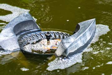 Water around Messner floating skimmer boils from air bubbles. Selective focus. Close-up. Skimmer floats on surface of water and collects leaves, dirt and other foreign objects from surface.