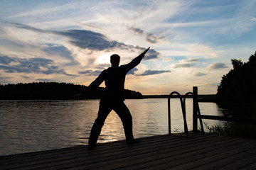 ein Mann steht bei Sonnenuntergang am See und macht Sport