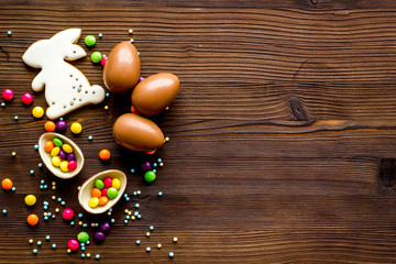 Sweet Easter symbols - chocolate eggs and bunny gingerbread - on dark wooden background top-down frame copy space