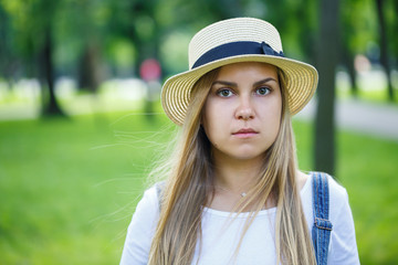 young beautiful girl in denim overalls and a light hat walking in the park