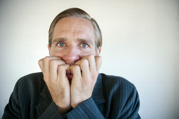 Nervous businessman biting his fingernails looking at the camera with a frightened expression