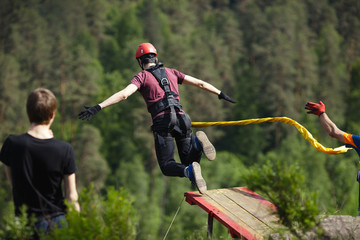 Extreme athlete, tied to a safety rope, jumped into the void after a take-off on a wooden platform,...