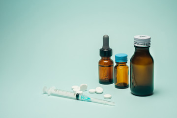 Objects of medical brown bottle, syringe and spilled pills on green teal table