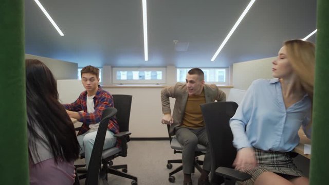 Tracking tilt up pov shot of team leader telling good news to colleagues and group of happy young office workers standing up and enjoying dancing at workplace celebrating success