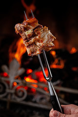 American cuisine. Fried pork ribs with honesty, chopped on a fork against a fire. The cook holds a fork in his hand. background image, copy space text