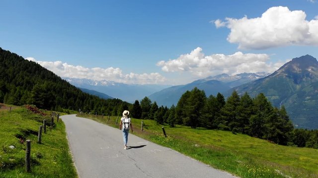 Young female hiker with backpack and in hat walking on path in mountain valley enjoy scenery of hills, woman wanderlust using mobile phone for making picture of beautiful nature landscape