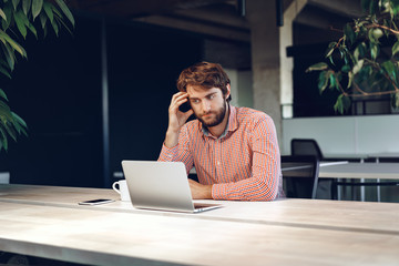 Puzzled thoughtful businessman sitting at his working table in an office. Business concept