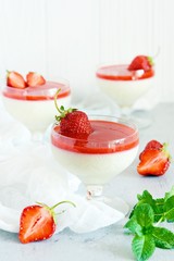 Delicious italian dessert panna cotta  with strawberry sauce, strawberries and fresh mint leaves. Summer creamy dessert with berries and mint in a glass on a light background.
