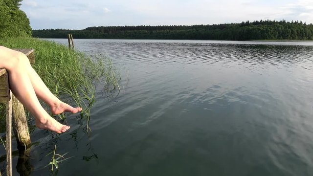 eine Frau sitzt am See und l&auml;sst die Beine h&auml;nge