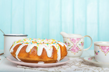Easter cake on a plate, tea, cream, colorful eggs on a blue background, Easter celebration concept