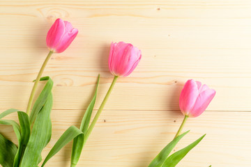 Top view of three small vivid pink tulip flowers and green leaves on a raw wooden table, beautiful indoor floral background photographed with small focus