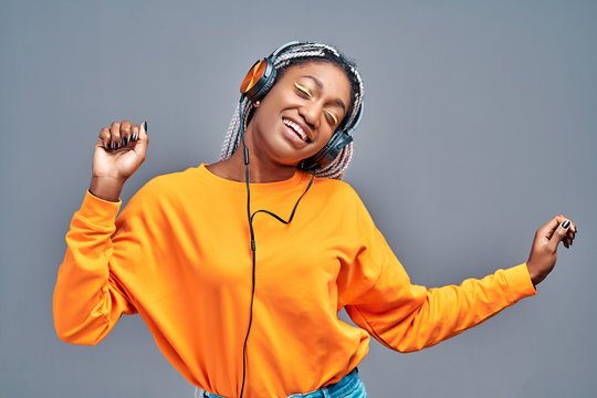 Afro woman in headphones listening to music and dancing over grey studio background