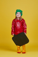 Little child girl holding black chalkboard banner on yellow background. Funny Face. Copy space for text. Advertising seasonal childrens products