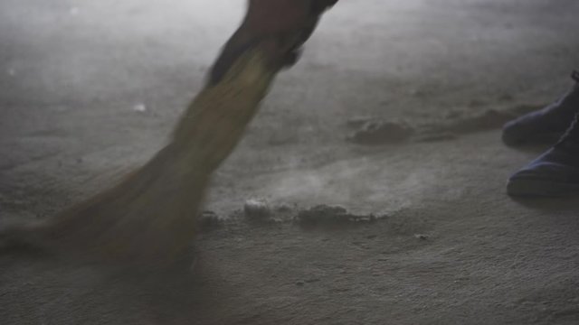 Worker sweeping adusty concrete floor close-up