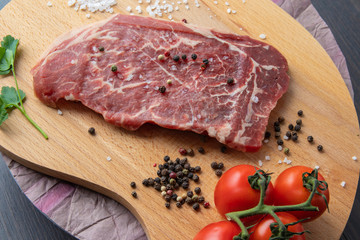 Raw beef steak with spices on a dark board. View from above.