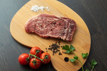 Raw beef steak with spices on a dark board. View from above.