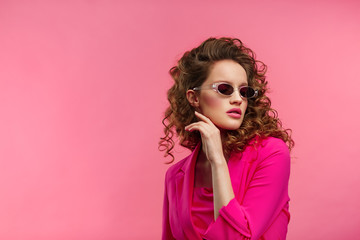 Close up fashion studio portrait of young beautiful women with curly hair.Nice girl with wavy hairstyle,bright make up and stylish eyeglasses isolated over pink background.Beauty and hair care concept