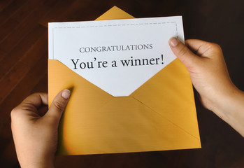 An open shiny gold envelope with a letter that says Congratulations You're a winner! with female...